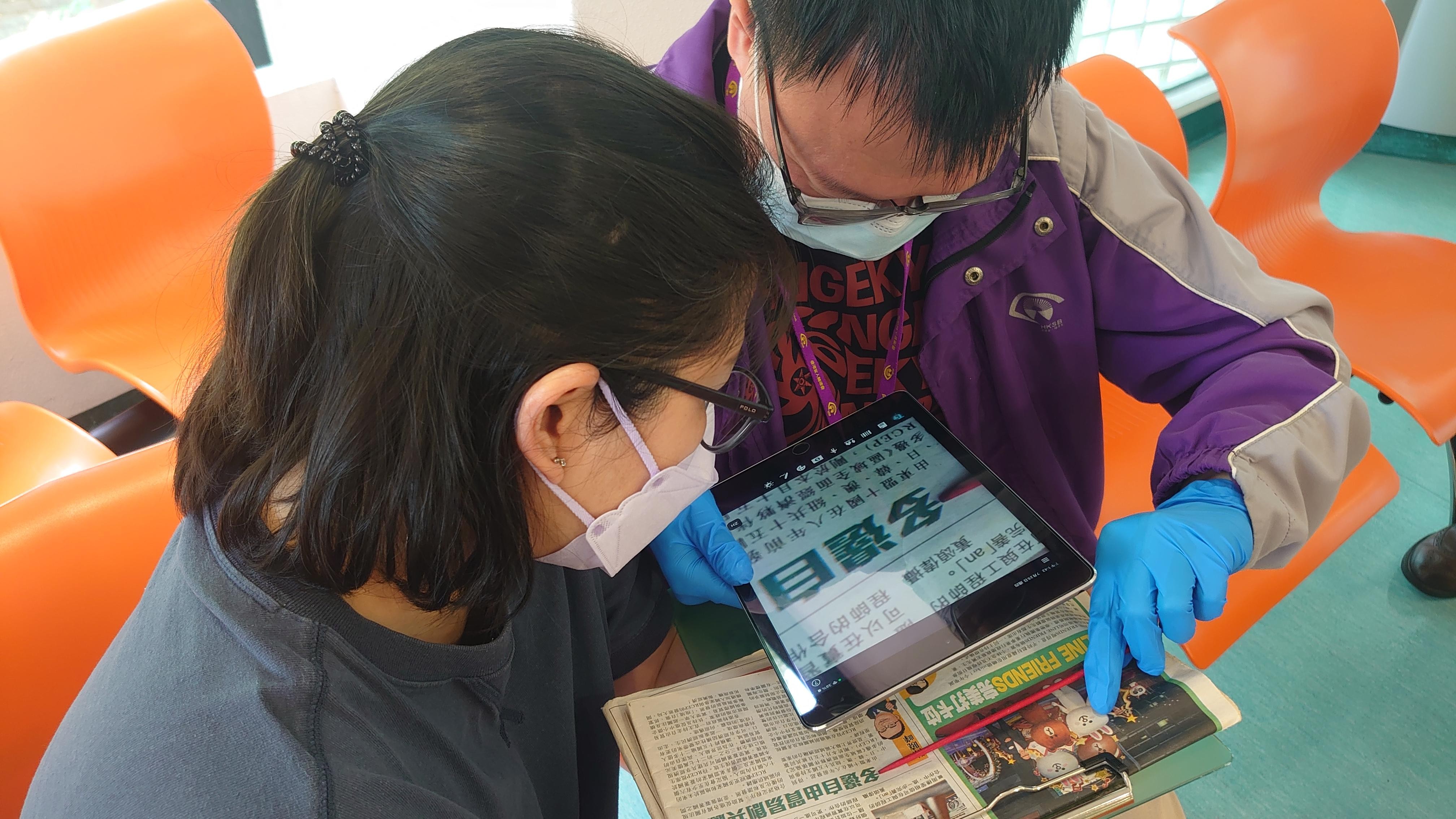 診所助理利用診症大堂的WIFI無線上網功能，向視障人士示範如何使用平板電腦電子放大功能。